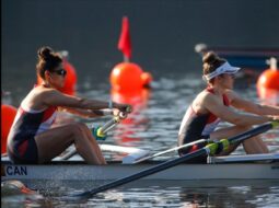 American rowing team preparing to race at a Canadian regatta on a calm lake with Canadian flags in the background.