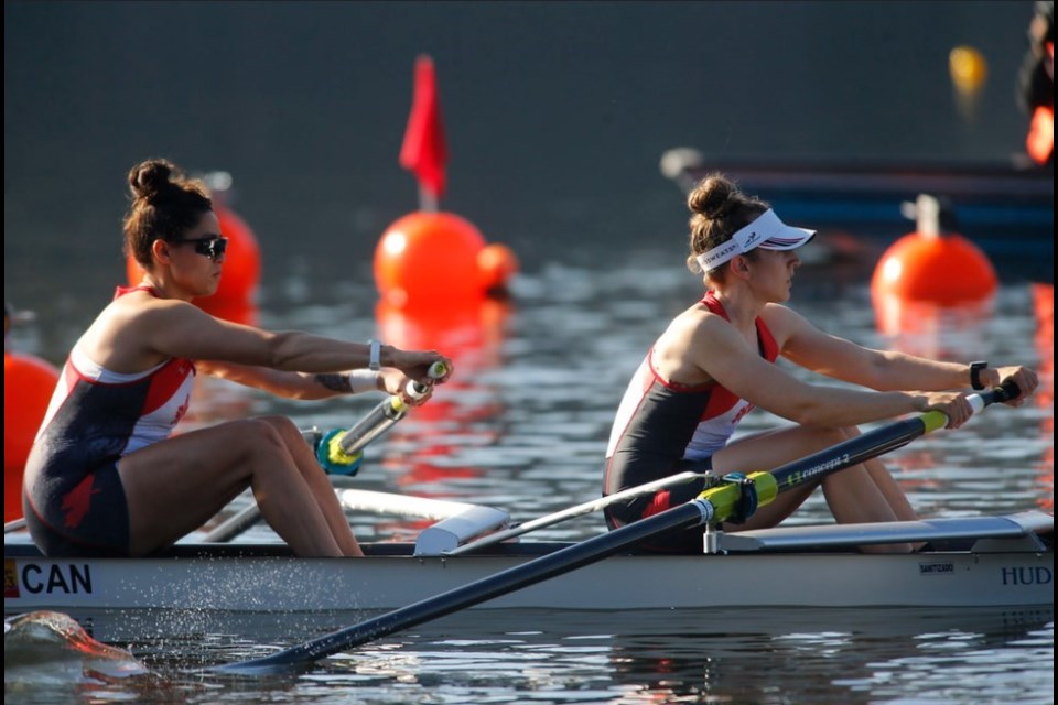 American rowing team preparing to race at a Canadian regatta on a calm lake with Canadian flags in the background.